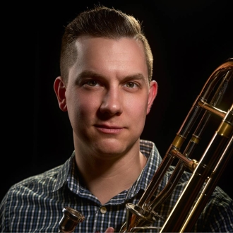 Headshot of a white man with brown hair, holding a trombone.