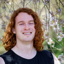 A smiling person with red hair against a floral background