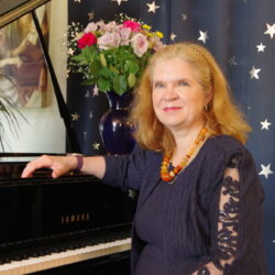 A woman sits at a piano in front of a curtain printed with stars