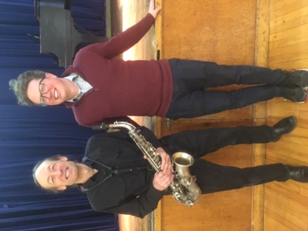 The story protagonist, Marc, holds a saxophone and smiles while standing next to his teacher. 